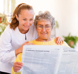 Caregiver and Elderly Woman Reading a Newspaper